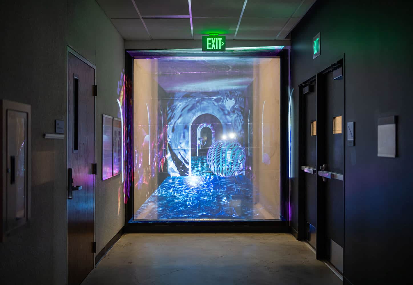 At the end of a hallway, a video is projected onto a floor-to-ceiling scrim. The video depicts an arched doorway in a blue, fragmented atmosphere.