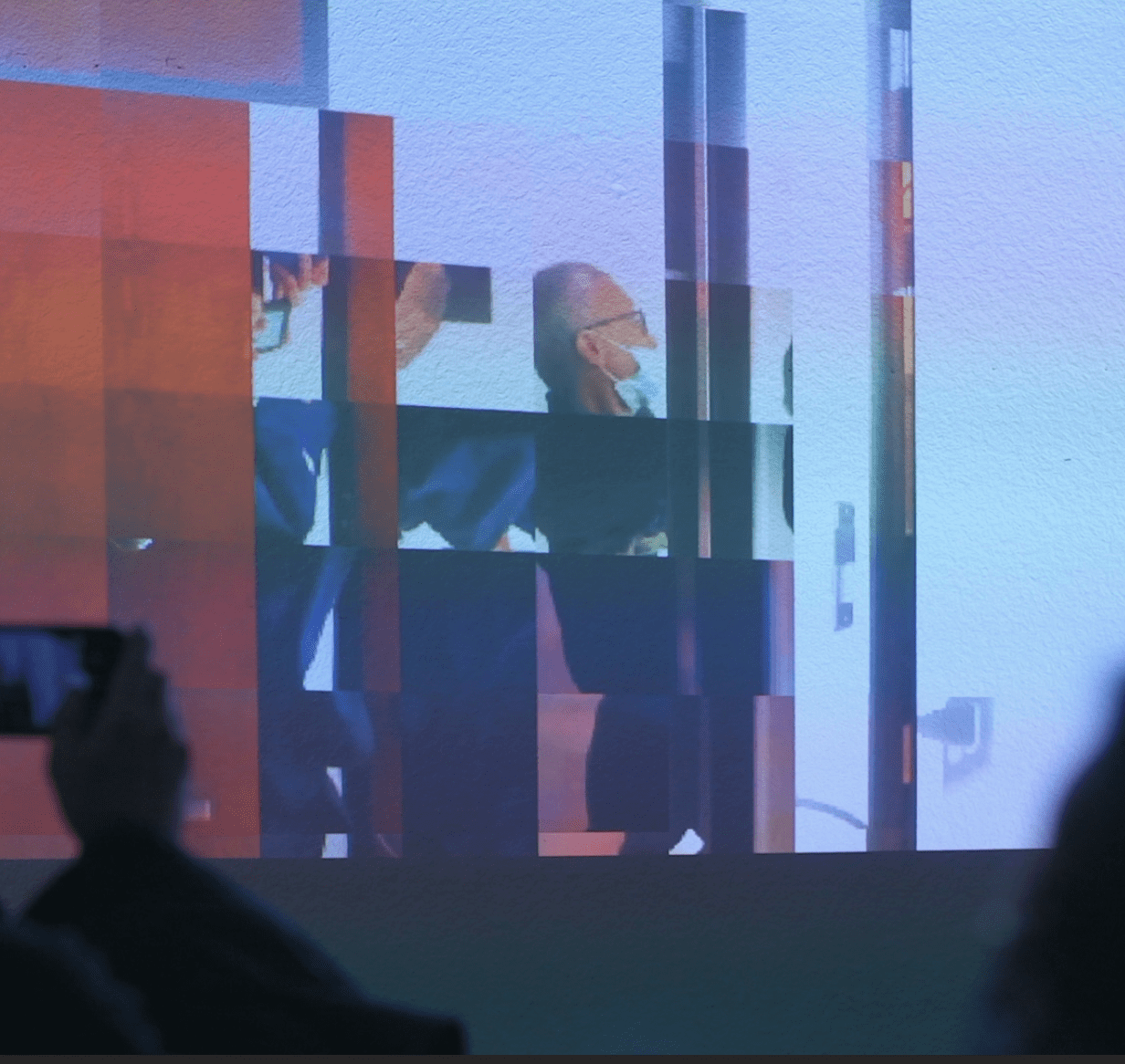 A fragmented video is projected onto a wall. The video displays life video from the room, shattered in a grid pattern, and sometimes mirrored.