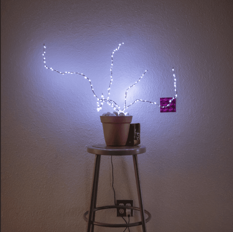 A small plant pot stands on a stool. Led lights in the shape of branches are placed in the plant pot.