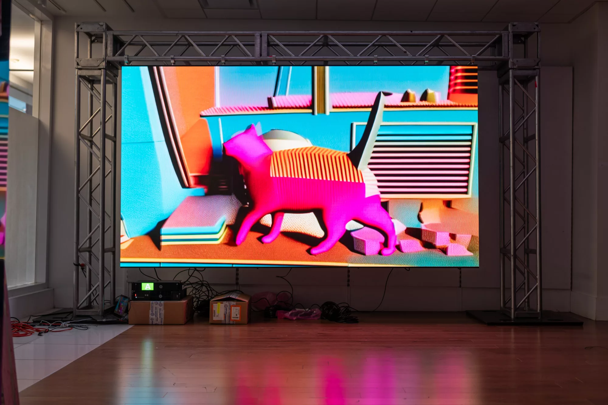 A video wall is hung on a metal trellis. The video is AI driven, brightly colored (primarily pink, orange, and blue) footage of a cat.