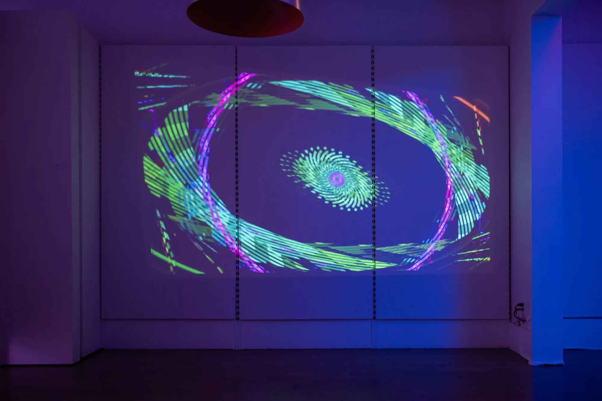 A projected video with abstract patterns in blue, purple, and green. The lines overlap and curve into a pointed oval. A second oval sits in the middle, like a pupil and iris of an eye.
